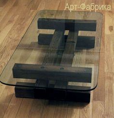 a glass coffee table with wooden legs and a square shaped design on the top, sitting on a hard wood floor