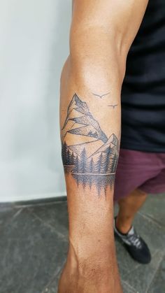 a man with a mountain tattoo on his arm and foot is standing in front of a wall