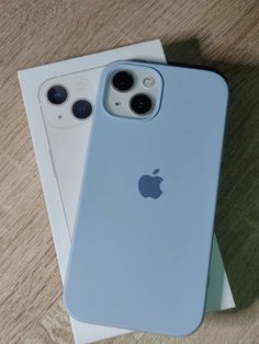 two iphones sitting next to each other on top of a wooden table in front of a box