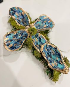 a cross made out of blue glass and moss on a white counter top with gold accents