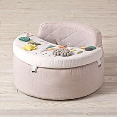 a round ottoman with toys on it sitting on a wooden floor in front of a white wall