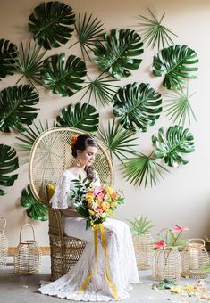 a woman sitting in a chair with flowers and greenery on the wall behind her