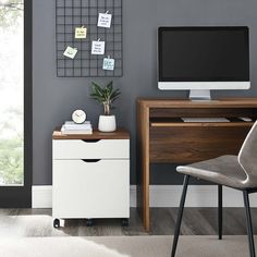 a computer desk with a monitor and keyboard on it in front of a gray wall