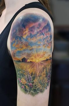 a woman's arm with a colorful sunset and clouds tattoo on her left shoulder