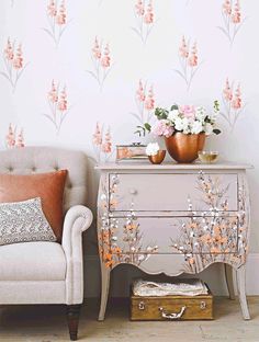 a white chair sitting next to a gray table with flowers on it and a pink flowered wallpaper