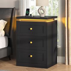 a black night stand with three drawers and a lamp on the nightstand next to it