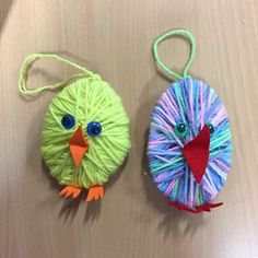 two ornaments made to look like birds with yarn on their backs and feet, one is green and the other is blue