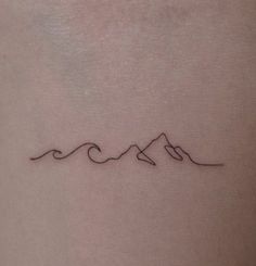 a small wave tattoo on the back of a woman's left arm, with mountains in the background