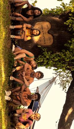 a group of young people standing next to each other in front of a large tree