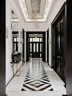 an elegant hallway with black and white flooring, chandelier and two doors