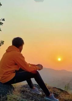 a man sitting on top of a hill at sunset