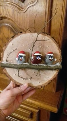 a hand holding a piece of wood with three little owls on it and one is wearing santa's hats