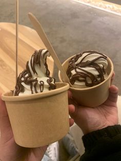 two ice cream sundaes with chocolate drizzled on top in paper cups