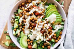 a salad with avocado, tomatoes, chickpeas and dressing in a white bowl