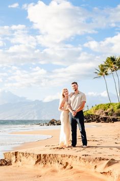 a man and woman standing on top of a sandy beach next to the ocean with palm trees