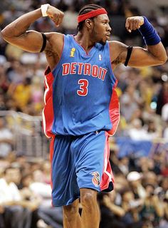 a man in blue jersey and red headband holding his fist up while standing on a basketball court