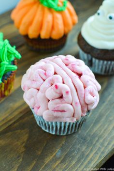 three cupcakes with frosting and sprinkles in the shape of a brain