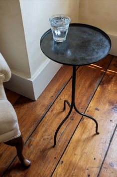 a glass sitting on top of a table next to a white chair and wooden floor