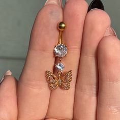 a woman's hand holding a gold butterfly belly ring with two diamonds on it