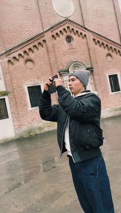 a man standing in front of a brick building taking a photo with his cell phone