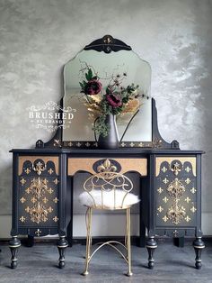 an ornate black and gold desk with mirror on top, flowers in vase next to it