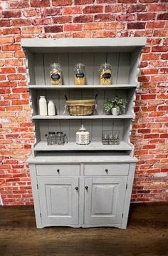 an old gray painted china cabinet in front of a brick wall