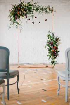 two chairs are set up in front of a white brick wall with flowers and greenery