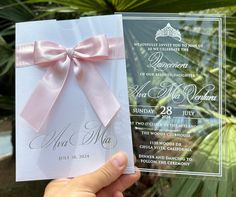 a hand holding up a wedding card with a pink bow on it and the front