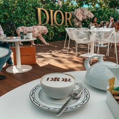 a white table topped with cups and saucers filled with food next to a sign that reads dior