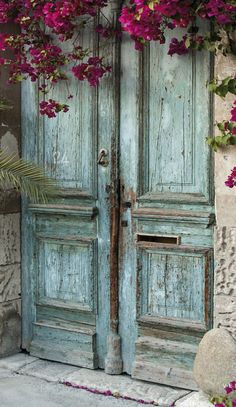 an old blue door with pink flowers growing on it's sides and over the top