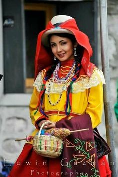 a woman dressed in colorful clothing holding a basket and smiling at the camera while standing next to a pole