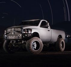 a white truck parked on top of a field at night with lights in the background