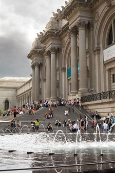 many people are sitting on the steps near water fountains