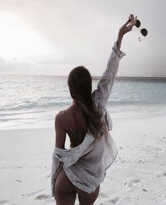 a woman is walking on the beach with her arms in the air while flying a kite