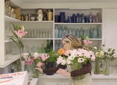 a woman arranging flowers in vases on the counter top at a florist shop