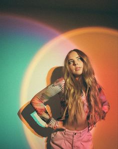 a beautiful young woman standing in front of a rainbow colored wall with her hands on her hips