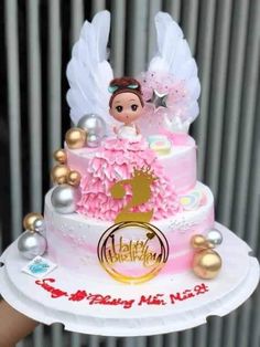 a pink and white cake with angel figurines sitting on it's top