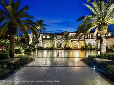 a large mansion with palm trees in the front yard and driveway area is lit up at night