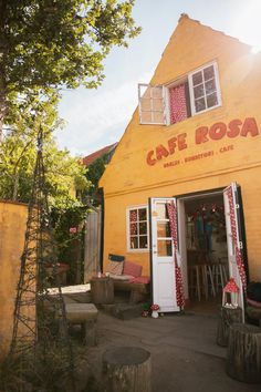 a yellow building with red and white curtains on it's front door that says cafe roa