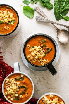 three bowls of tomato soup with macaroni and cheese on the side, along with spoons