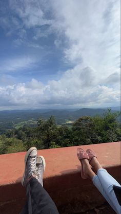 someone's feet on the edge of a wall with mountains and trees in the background