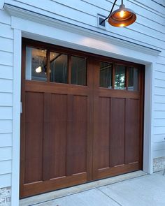 a brown garage door with two lights on the top and bottom side, in front of a white house