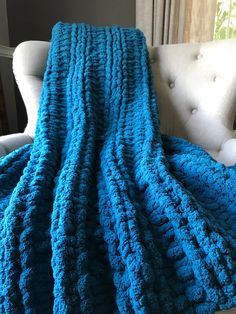 a blue crocheted blanket sitting on top of a couch next to a white chair