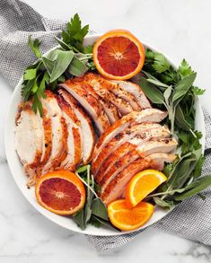 a white plate topped with sliced up turkey and oranges next to green leafy garnish