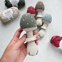 a hand is holding a crocheted doll in front of several skeins of yarn