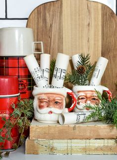 three ceramic santa claus mugs sitting on top of a wooden box next to christmas decorations