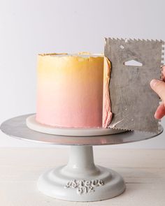 a person holding up a piece of paper next to a pink and yellow cake on a plate