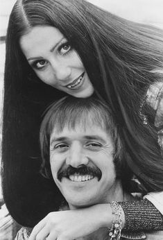 a man with long hair and a mustache is hugging a woman's head while they both have their arms around each other