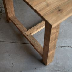 a wooden bench sitting on top of a cement floor next to a wall or window