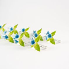 blue and green flowers are arranged on silver hair pins with leaves attached to the ends